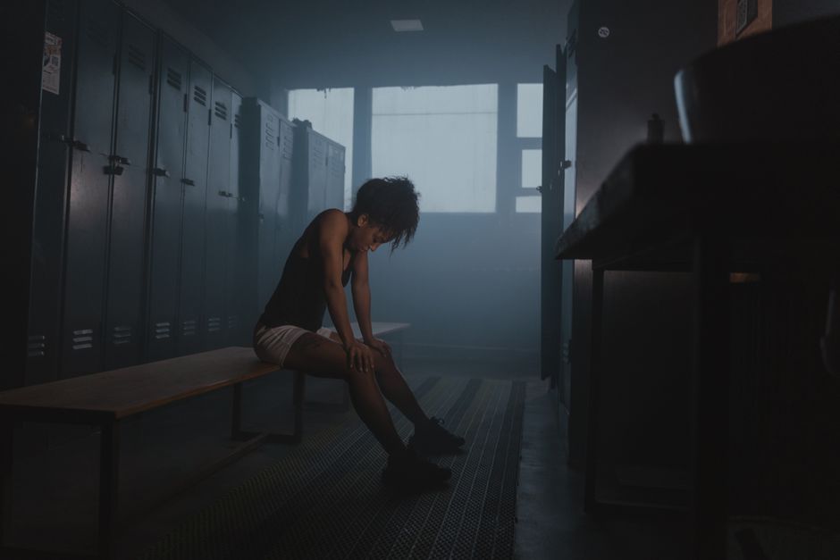 A tired athlete rests on a bench in a dim locker room, capturing a moment of reflection and exhaustion.
