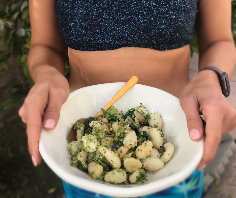Woman in athletic wear holding a healthy gnocchi bowl, perfect for a nutritious meal.